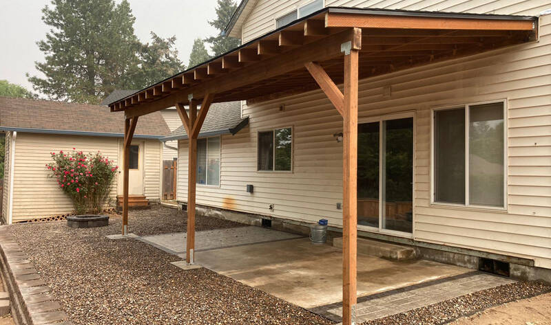 Alt text: Professional Awnings Installation by Timber Fence Construction with a wood patio cover supported by posts and braces beside a home.